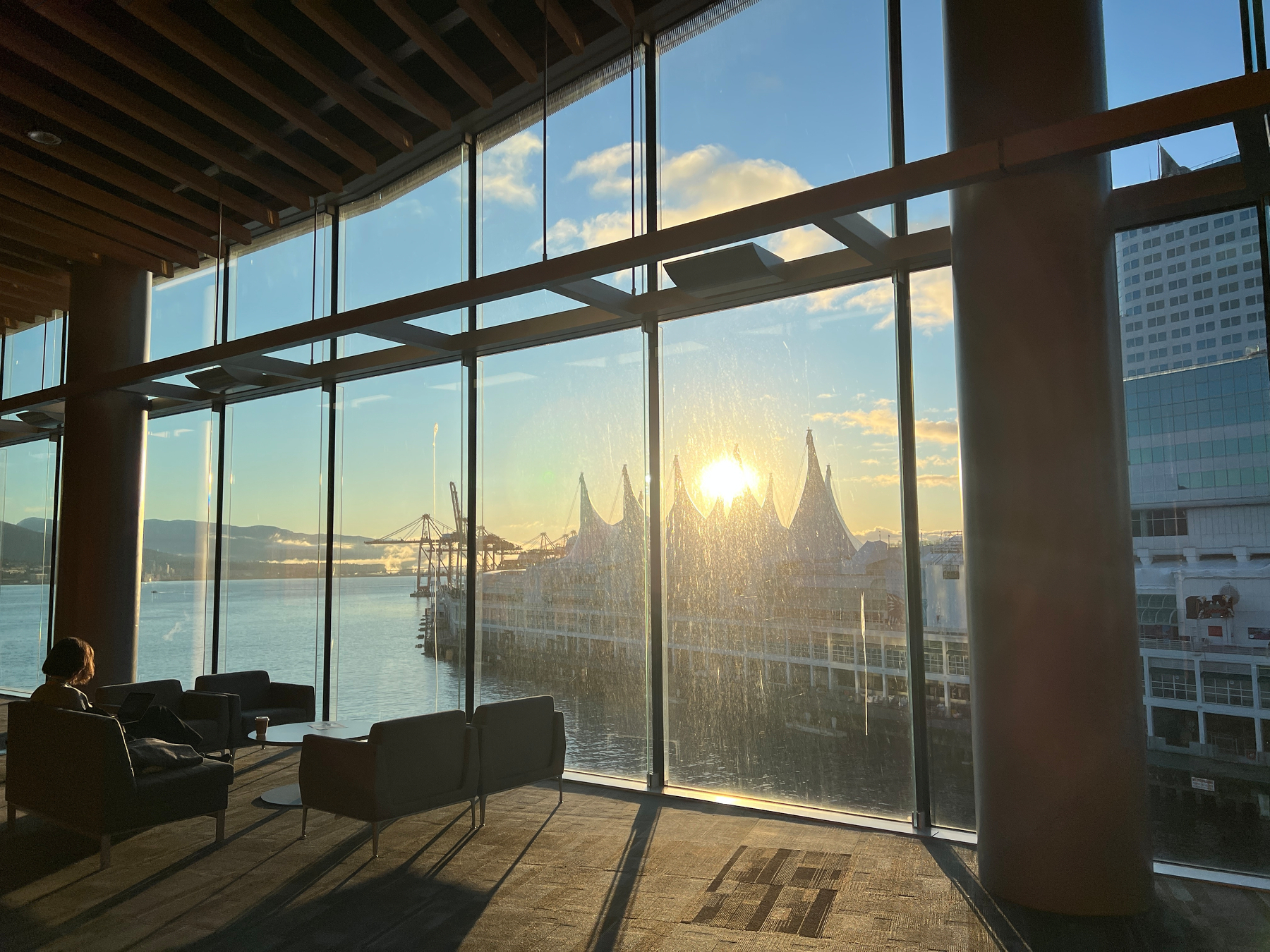 An early attendee sits in the bright sunlight at a couch in the VCC, looking at the sails of Canada Place where the morning sun is rising