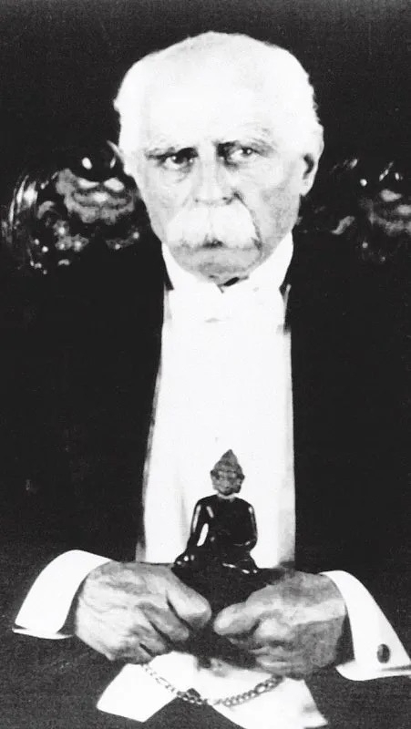 Image of Youngshusband with white hair and moustache holding a small statue of the Buddha