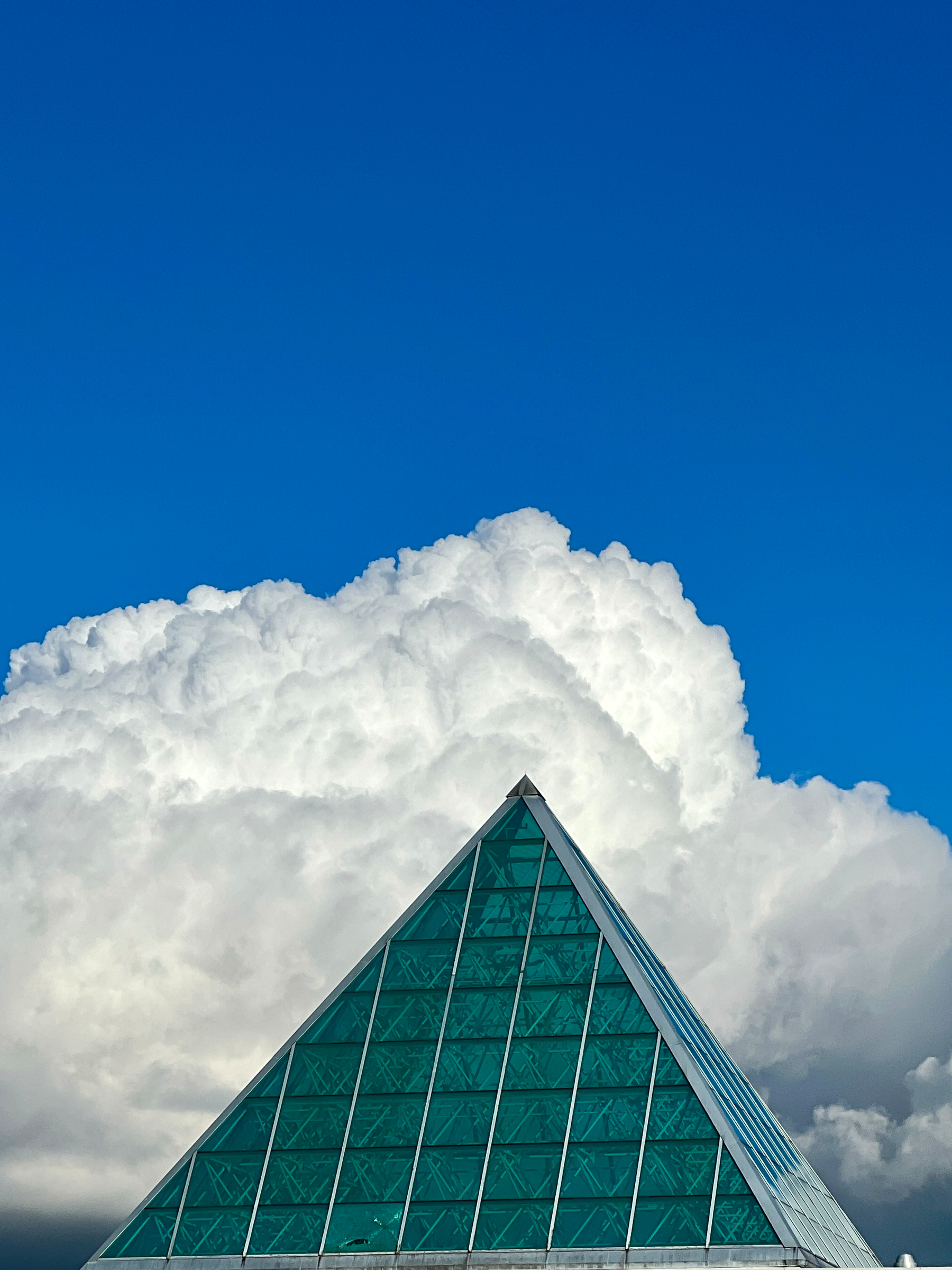 Bluey sky with billowing cloud. In the foreground is a glass pyramidal skylight from the top of a building