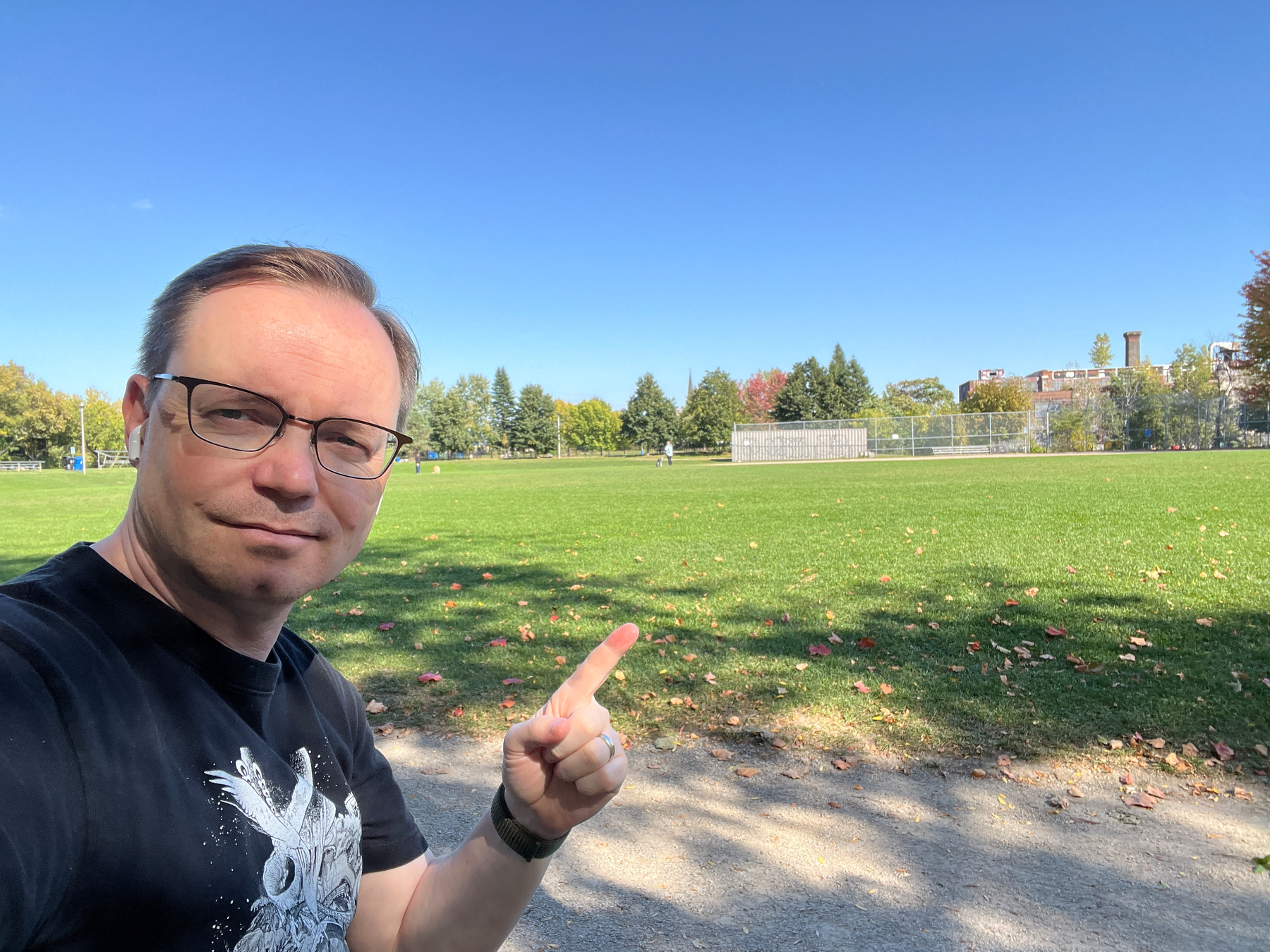  Sitting at a park bench, Chad points to a green field and baseball diamond at a local park. Above is a cloudless blue sky