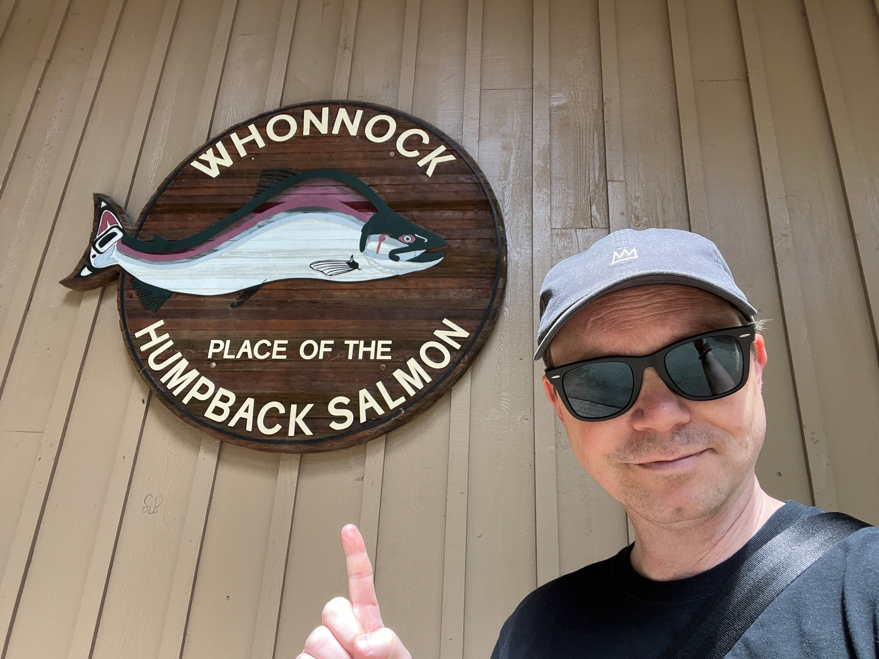 Chad points at a sign with the picture of a salmon and the words “Whonnock Place of the humpback salmon”