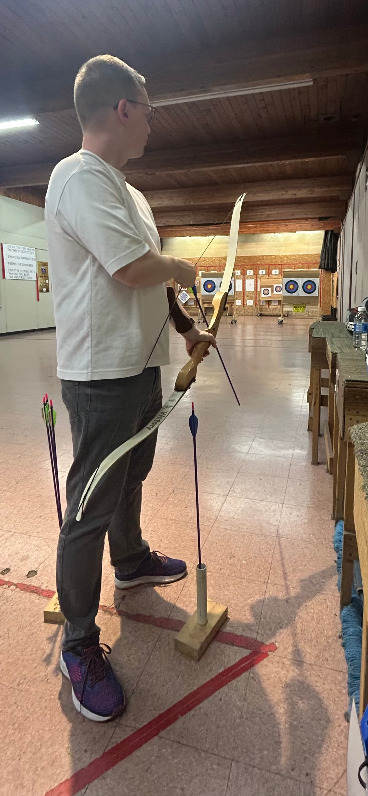 Chad stands about to raise his bow to shoot his second arrow