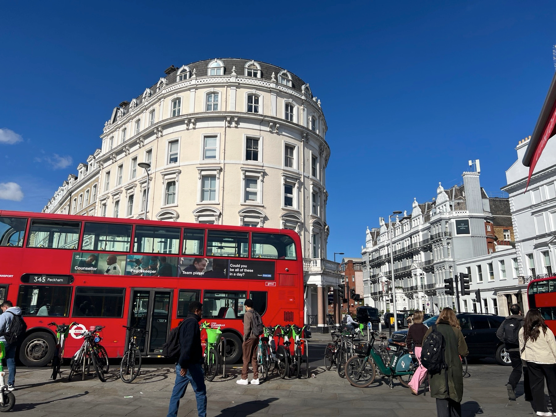 A bright red doubledecker in front of the bright white houses of South Kensington