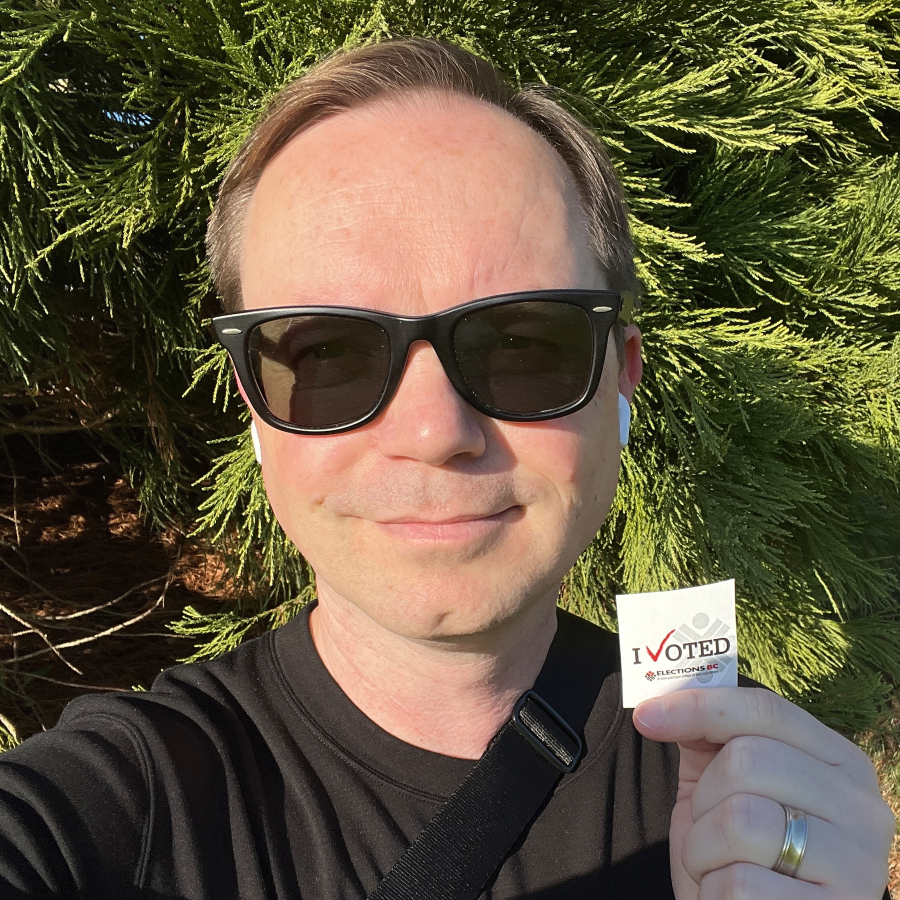 Chad wearing sunglasses facing the bright sun holds up an I VOTED sticker