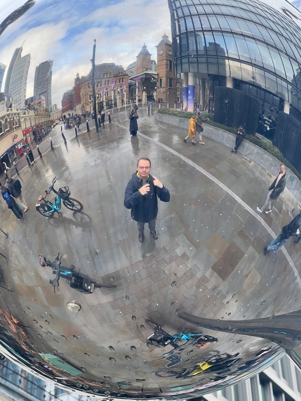 Reflected in a silver ball, Chad takes a photo pointing at himself