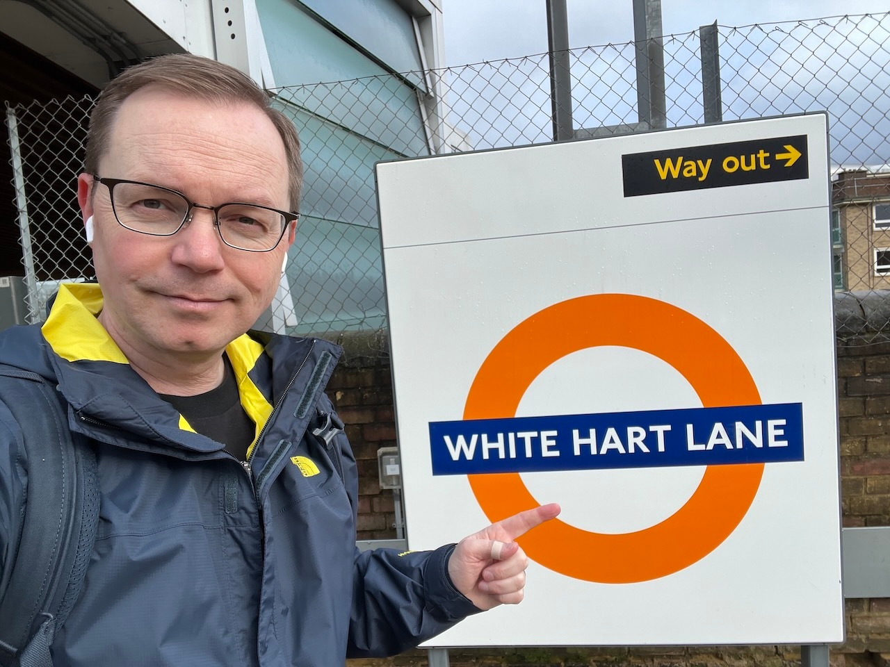 Chad points to the WHITE HART LANE train station sign (where the Tottenham Hotspur Stadium is)