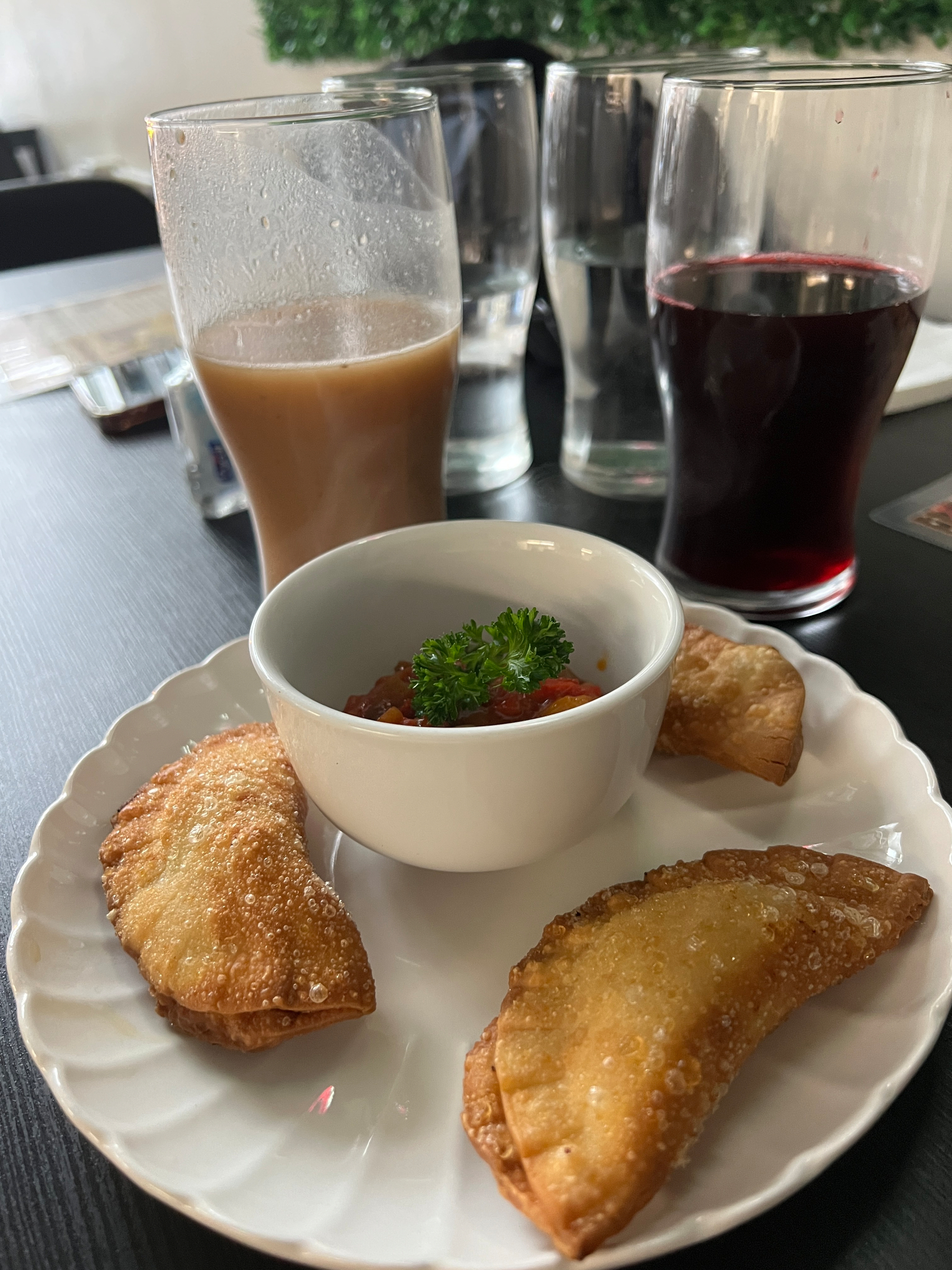 3 deep fried fataya with tomato sauce, a brown creamy drink (baobab), and a dark red drink (hibiscus)