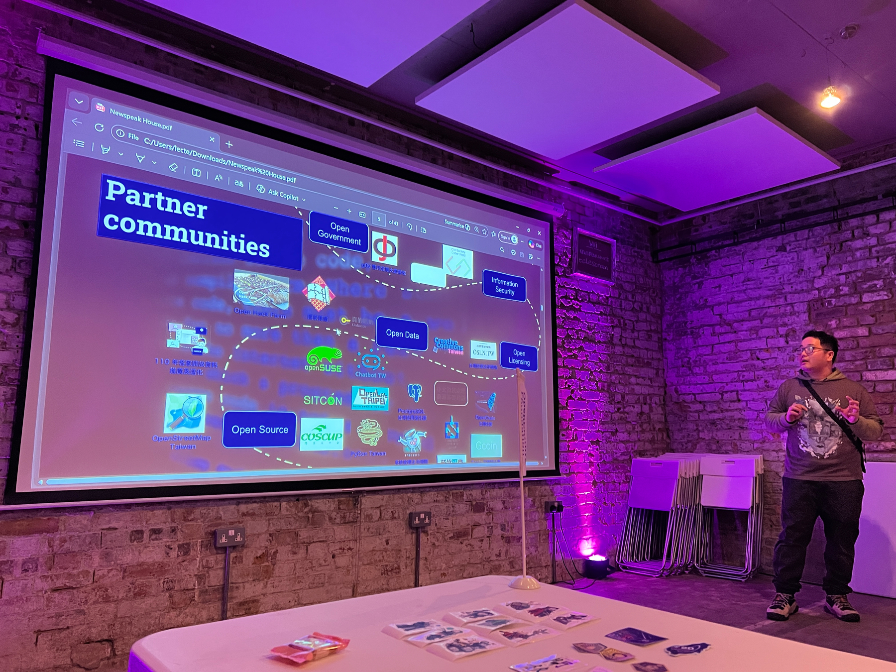 A presenter shows a slide on a projector screen outlining the 44 Taiwanese open source partner communities