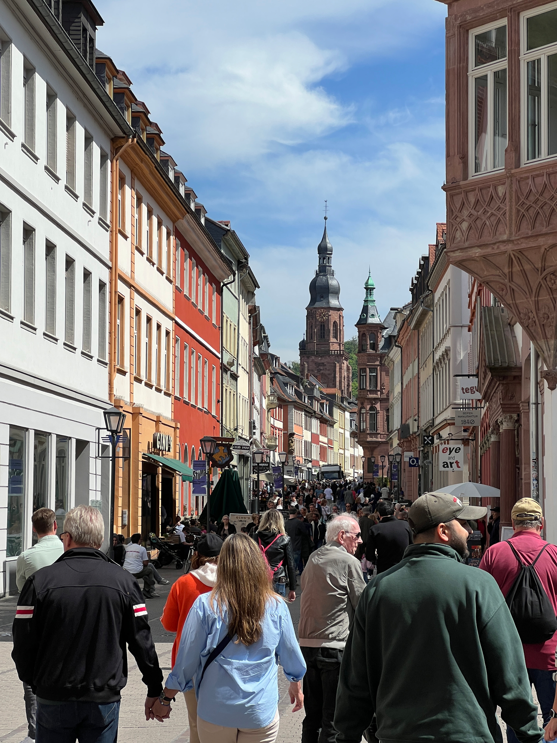 Crowded Heidelberg street in the old down. The spire of the Heiliggeistkirche pokes up above the rooftops in the distance