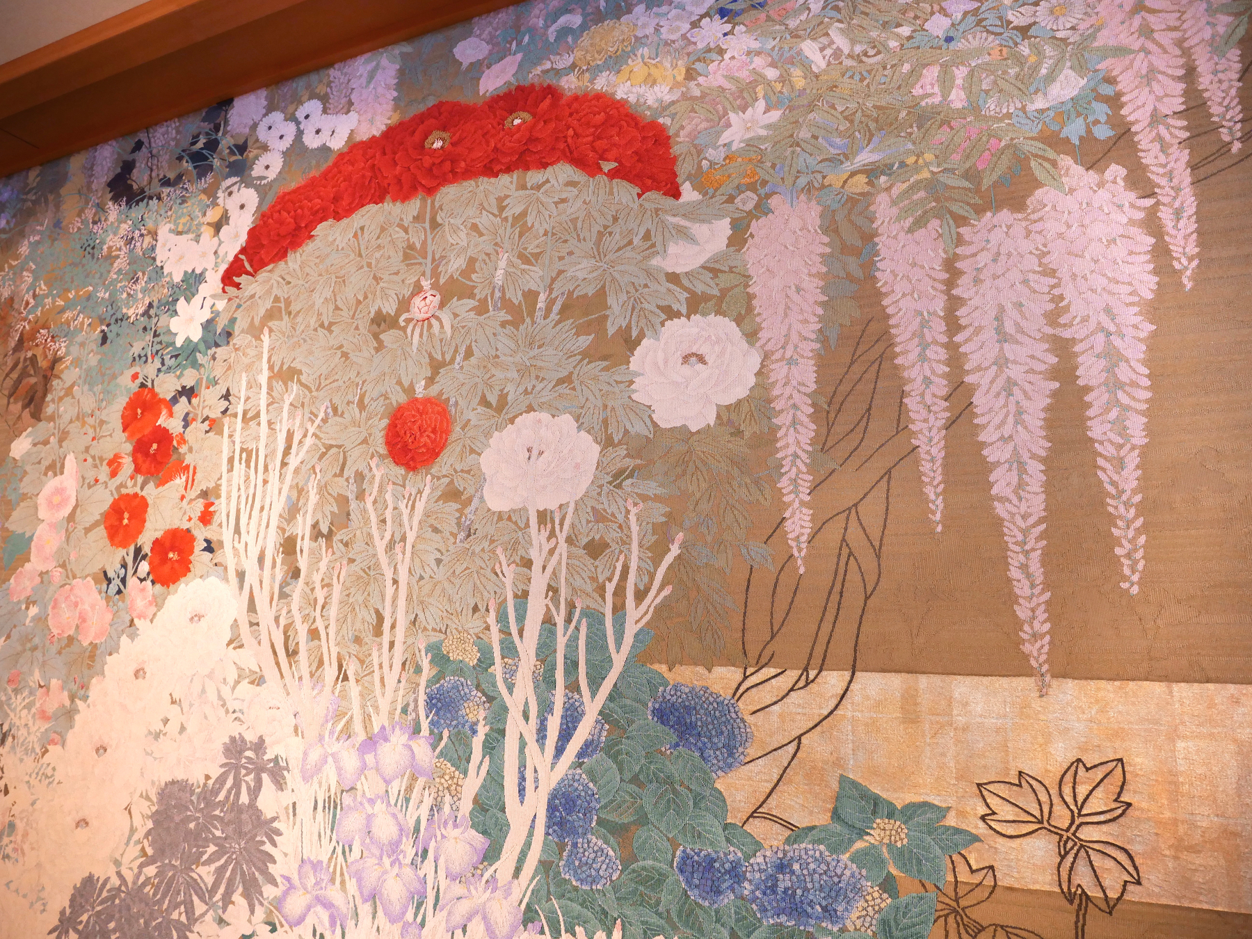 A vibrant and intricate tapestry showcasing various blooming flowers in shades of red, white, purple, and blue against a textured, multi-colored background.