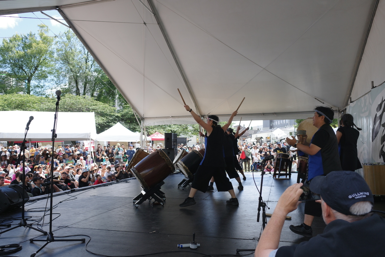 Japanese taiko drummers on a stage playing to a captive crown
