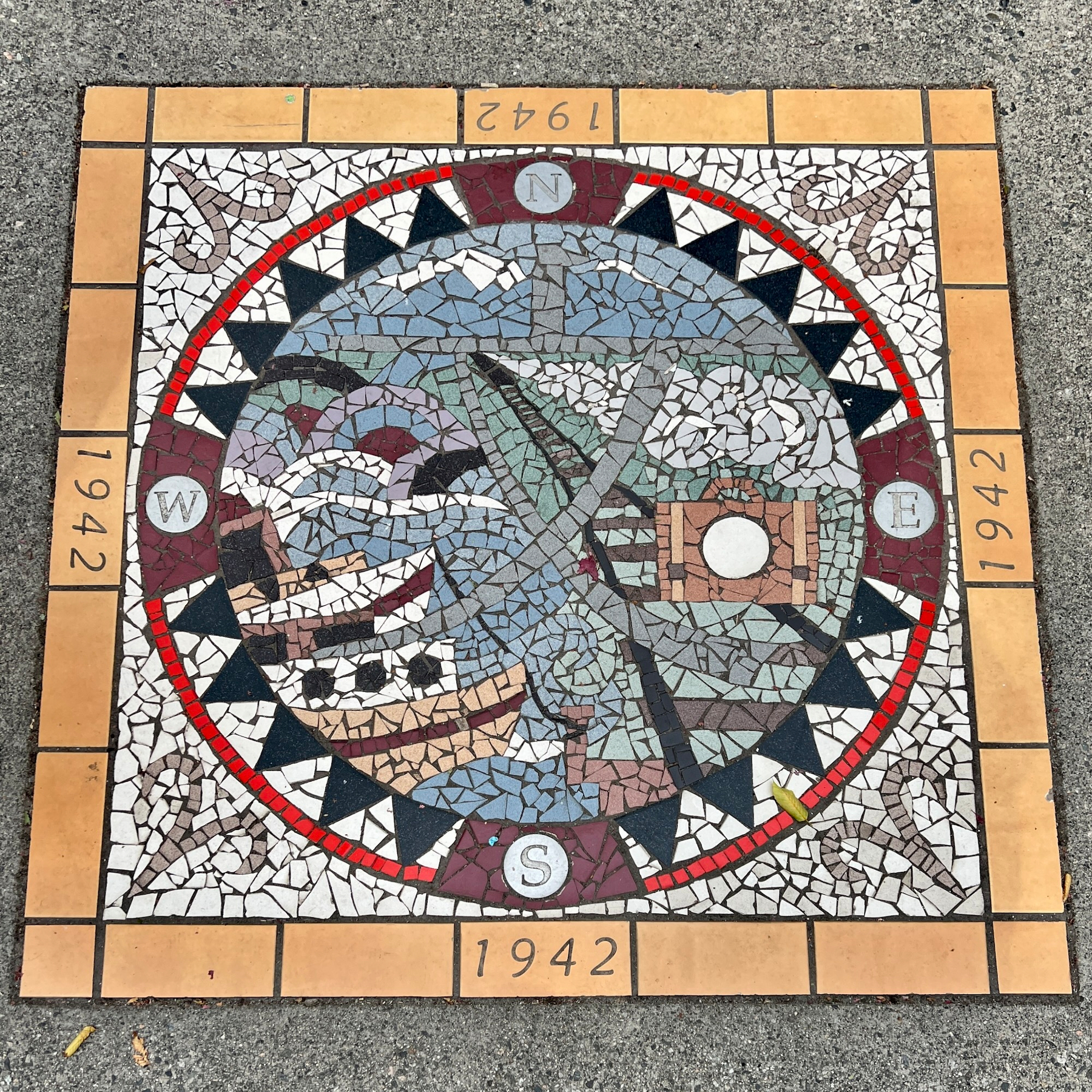 Mosaic depicting the 1942 internment featuring images of boats, railroads, a single suitcase, and the character 文 which is used on Japanese maps for school.