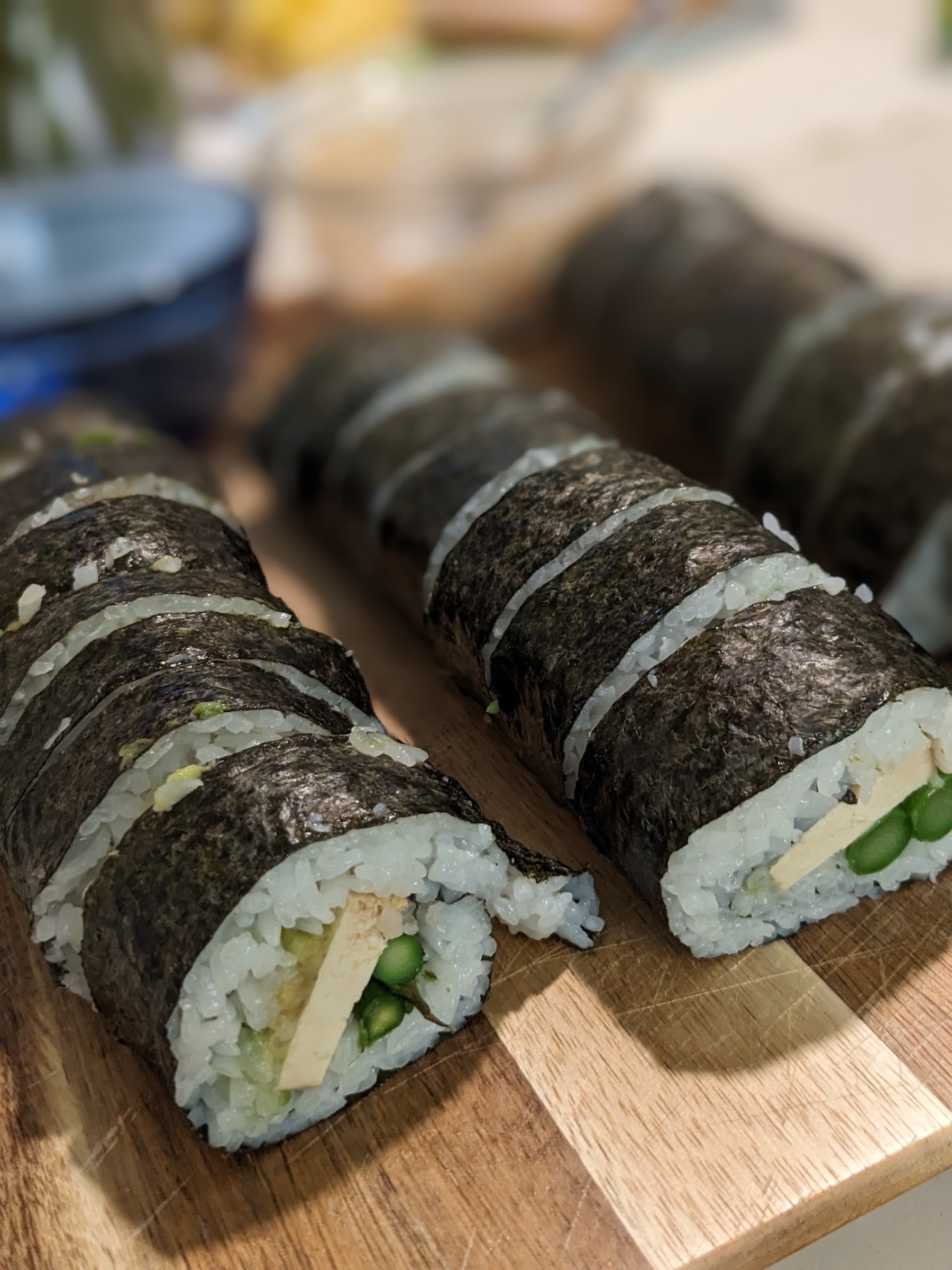 Three wide sushi rolls sit sliced on a wooden cutting board. The filling of asparagus, tofu, and avocado can be seen inside the rolls.