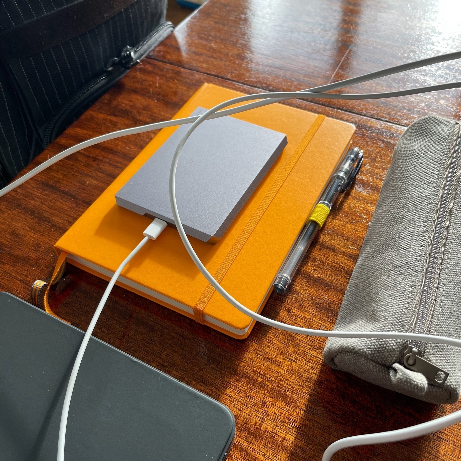 A yellow notebook, in which is sat a silver hard drive. There is also a tangle of white cables.