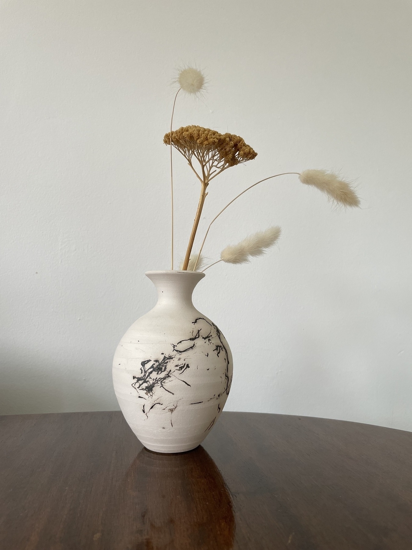 A dried flower arrangement in a naked raku bud vase.