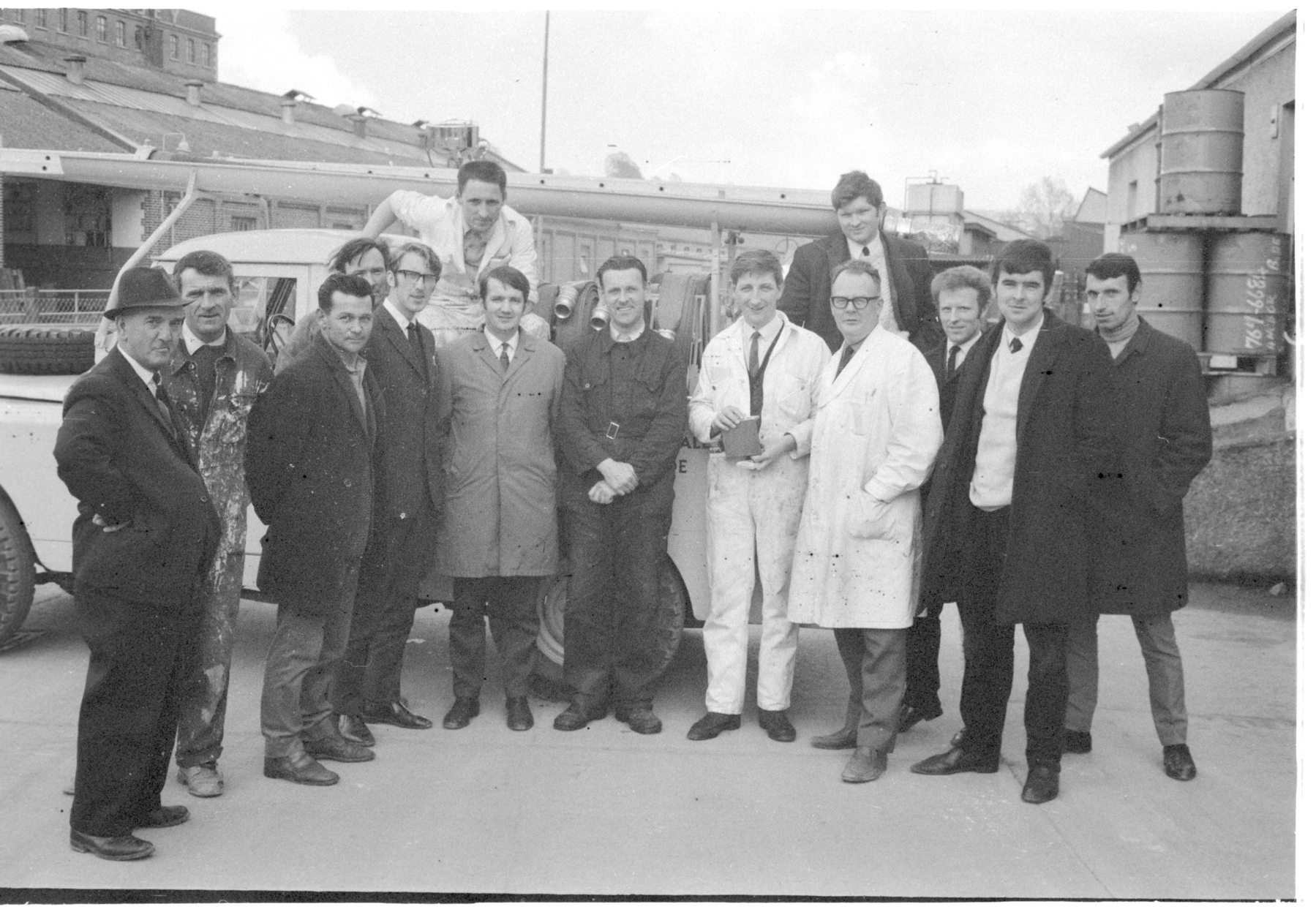 A group of people, some in work attire and laboratory coats, pose together outdoors in a black and white photograph.