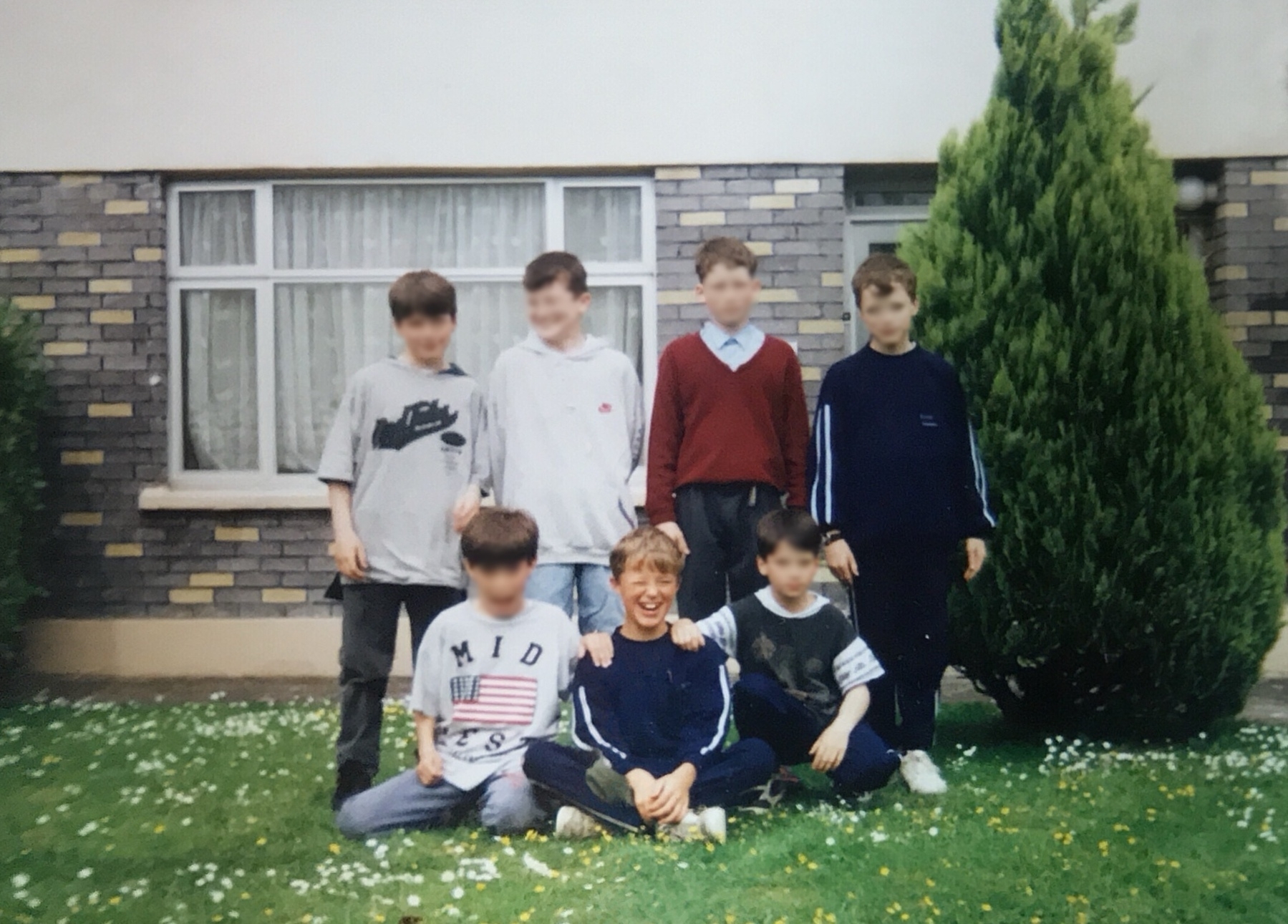 Auto-generated description: A group of six boys is posing together outside in front of a house.