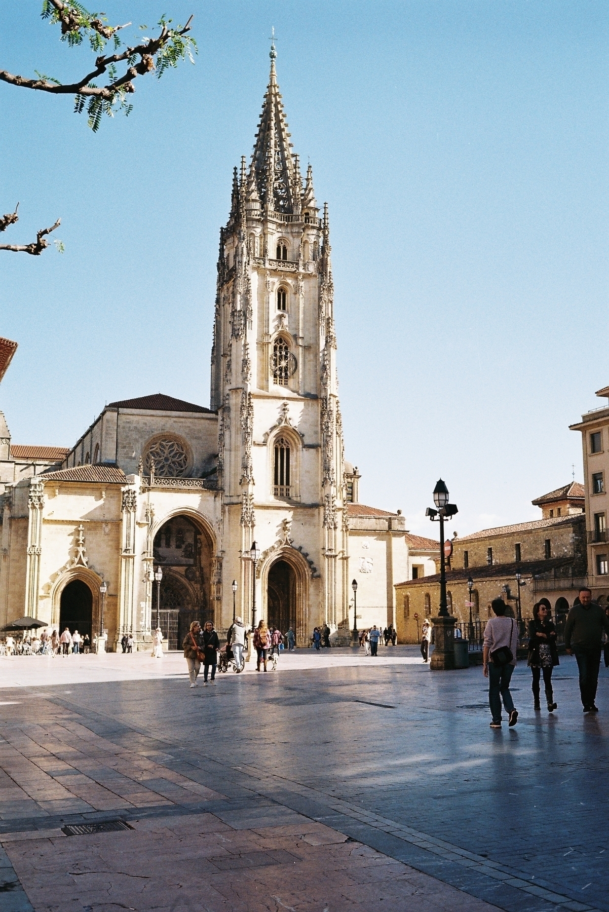 Auto-generated description: A Gothic-style cathedral with a tall spire towers over a plaza with people walking and enjoying the ambiance.