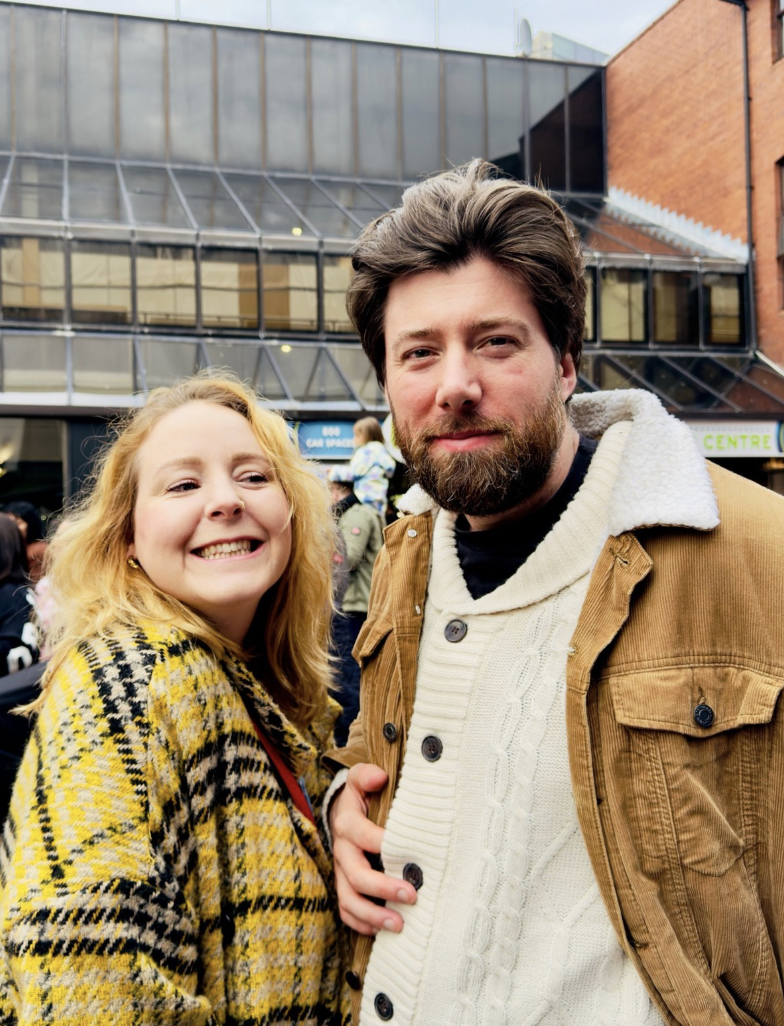 Auto-generated description: A woman and a man stand closely together, smiling, in an outdoor urban setting.