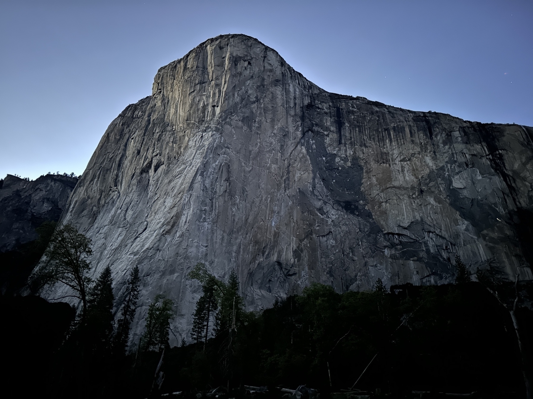 El Capitan. The largest rock on earth towers above Yosemite Valley, after sunset. The headlamp of a climber can be seen about halfway up on the eastern shoulder.