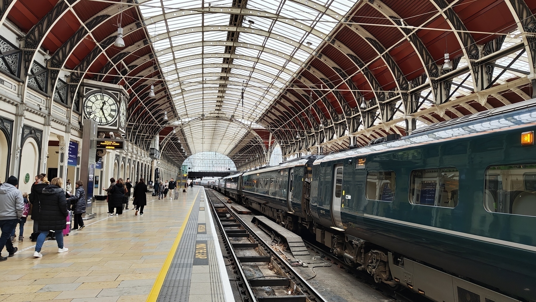 Looking along a train on Platform 2 to also show the arched roof railway station, with people walking along platform 1 towards the Paddington statue.