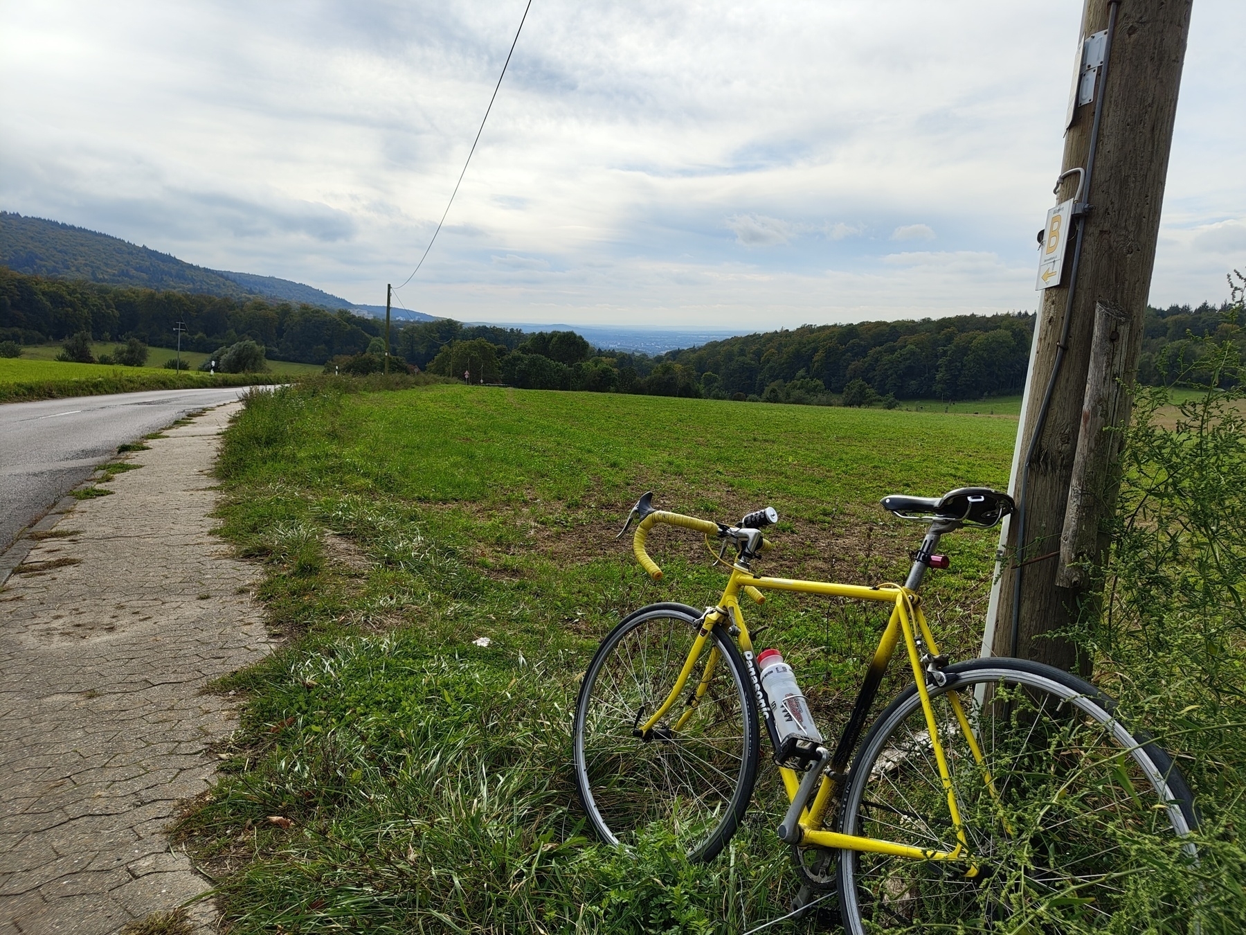 A yellow 1980s Panasonic road bike leaning against a telegraph pole at the top of a hill