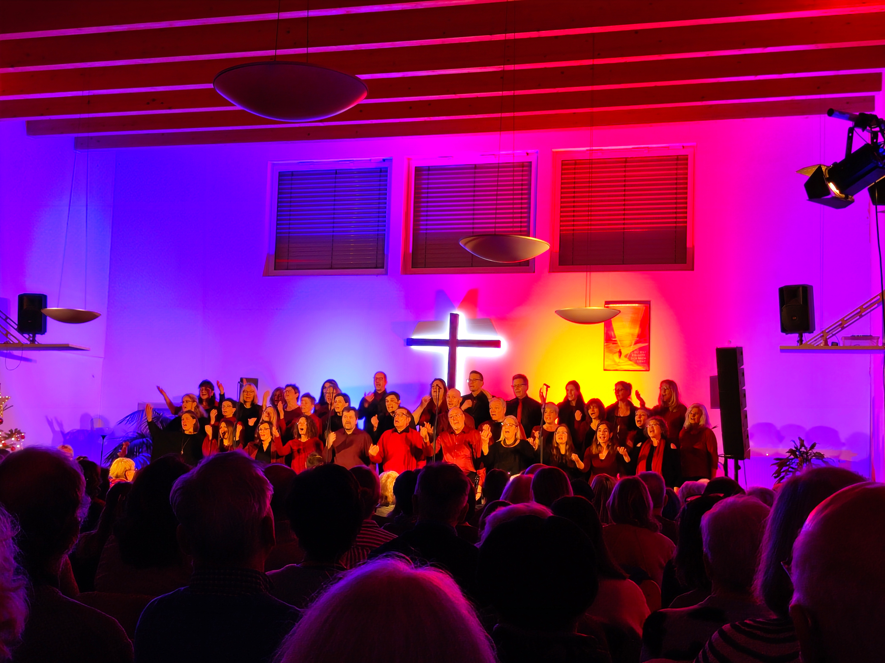 The Getogether gospel choir in front of a stark, modern black cross and a blue, red and yellow-green-lit wall