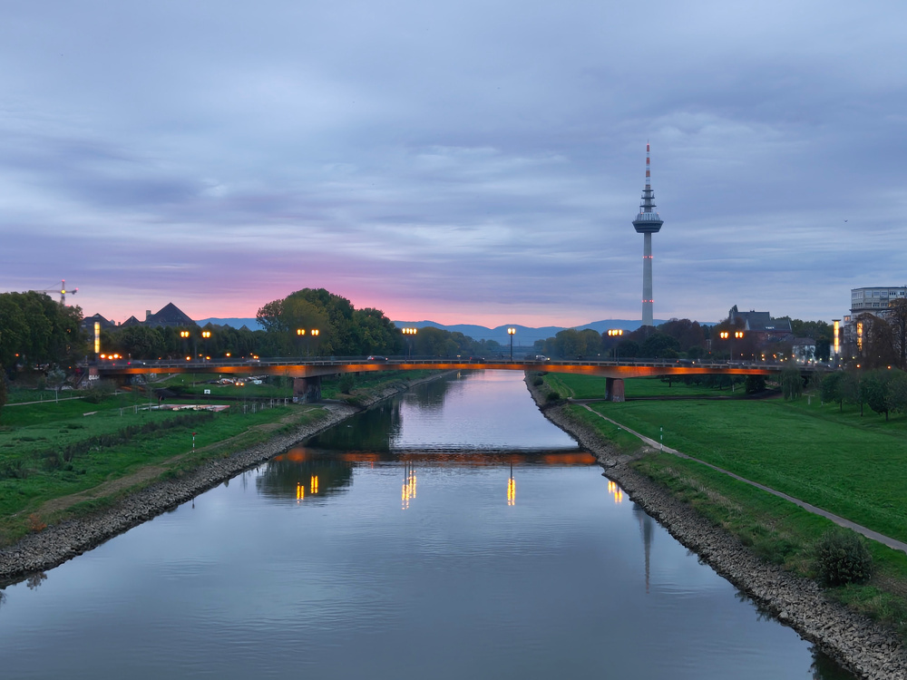 A peaceful river scene at dawn with a tower in the background and a bridge reflecting in the water.