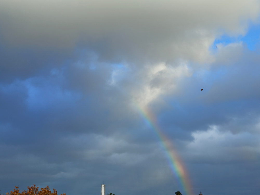 A cloudy sky features a vivid rainbow with a hint of blue appearing amidst the grey clouds.