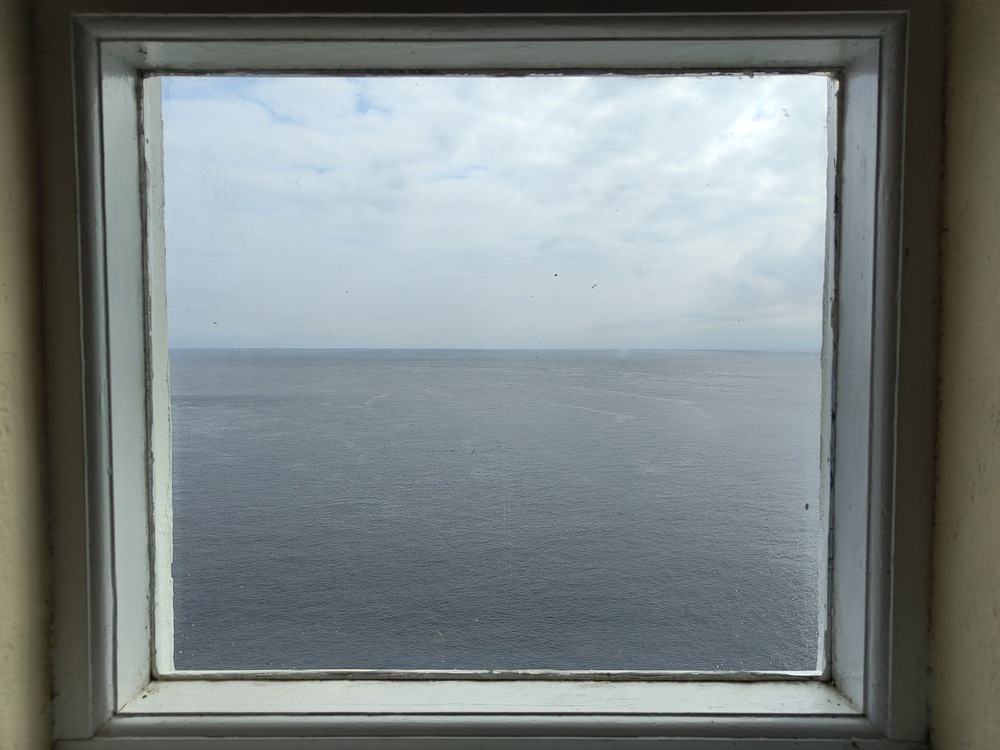 A window frames a view of the vast ocean under a cloudy sky.
