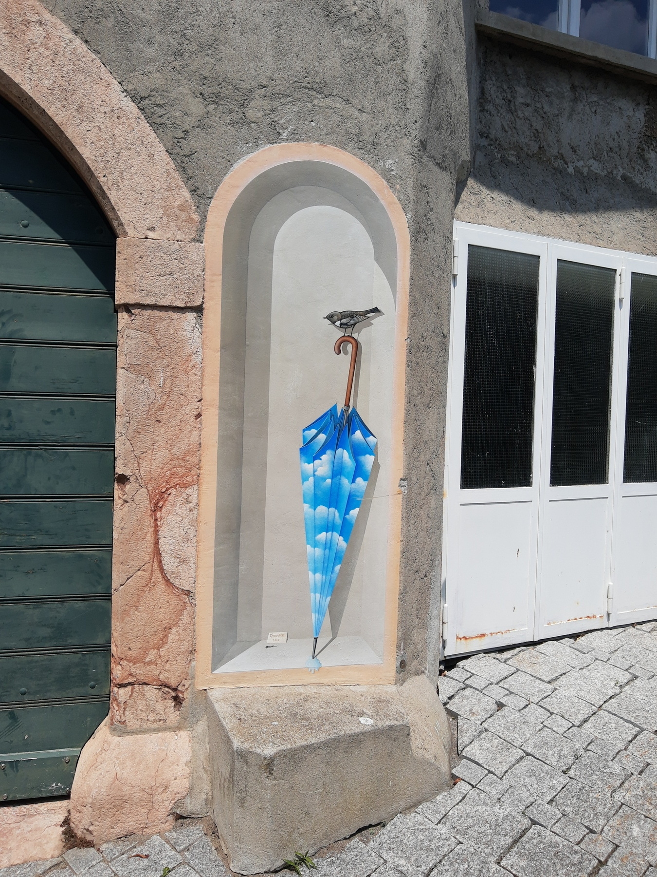 A paint on a wall showing a grey bird on a closed blu umbrella