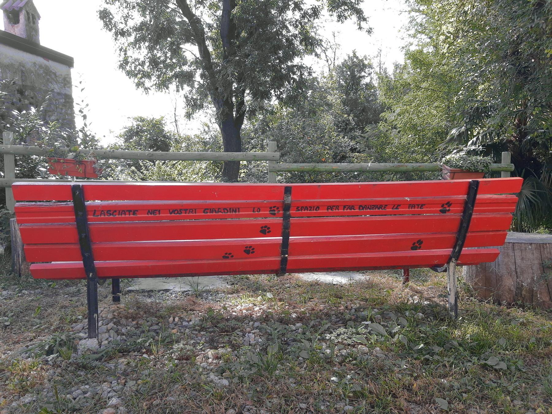 Panchina rossa con dietro una scritta: Lasciate nei vostri giardini lo spazio per far danzare le fate