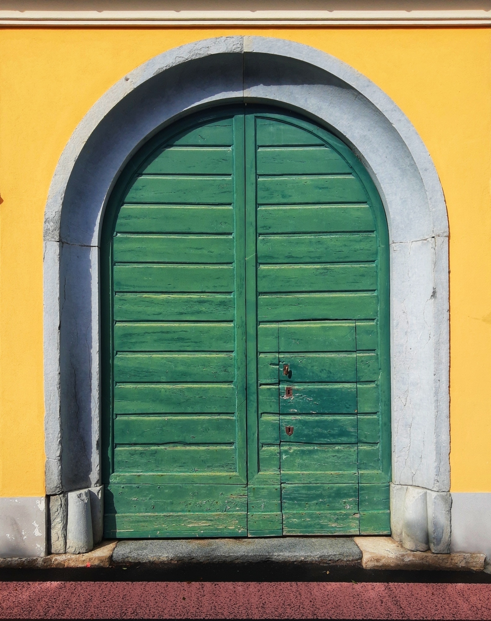 Auto-generated description: A large, arched green wooden door is set in a yellow-painted wall.