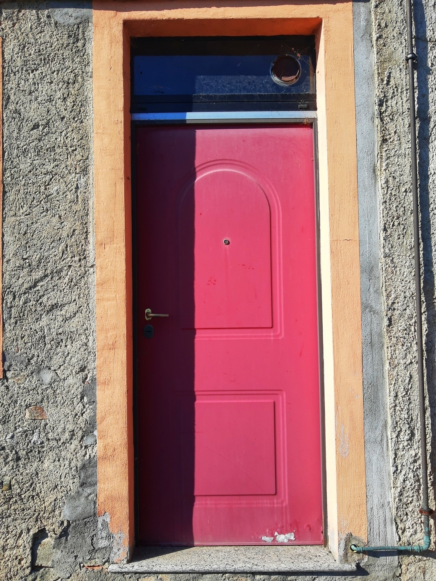 Auto-generated description: A bright pink door with a gold handle is set within a textured gray and orange frame.