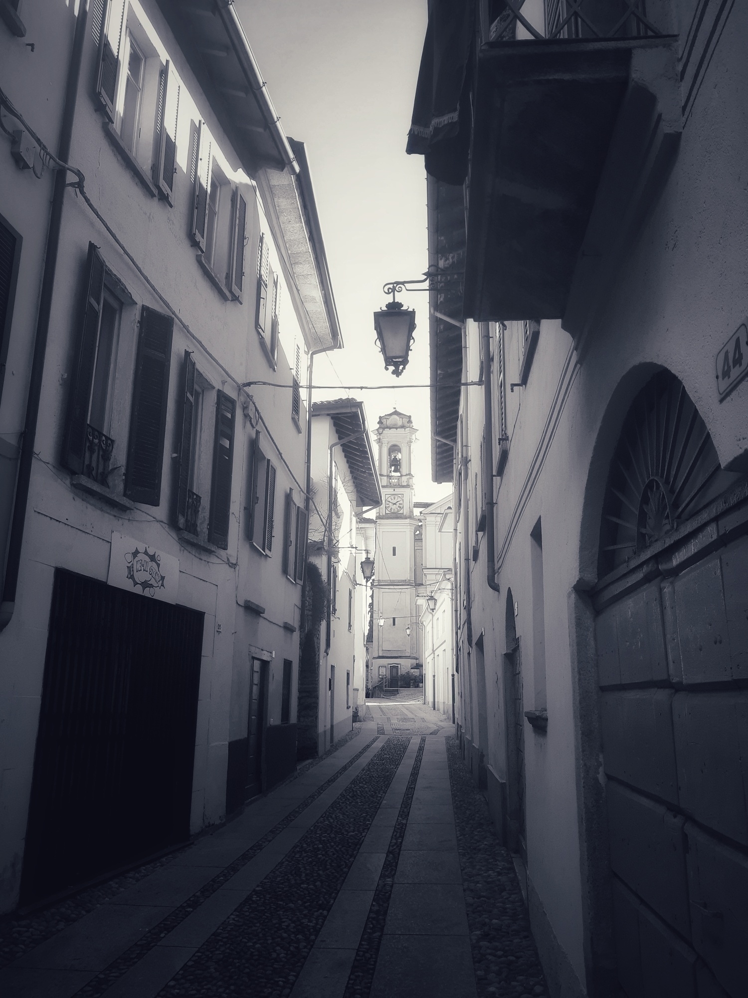 Auto-generated description: A narrow cobblestone street lined with historic buildings leads towards a distant church tower, bathed in soft, monochromatic hues.