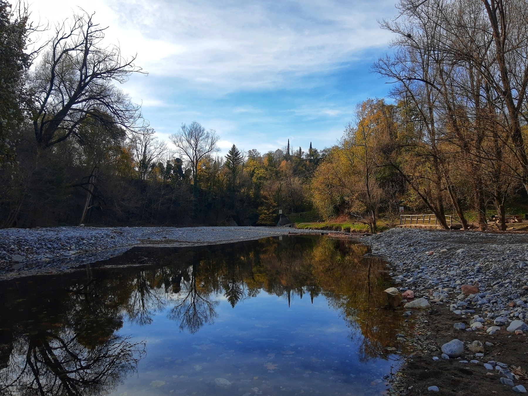 Auto-generated description: A tranquil river reflects the surrounding trees under a partly cloudy sky.