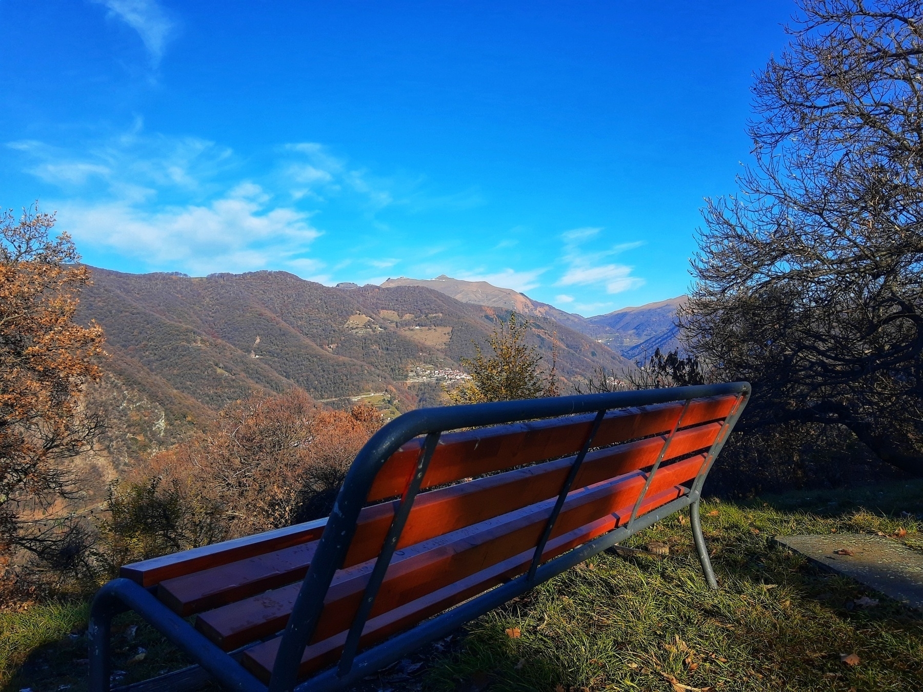 A red bench overlooks a picturesque mountain landscape under a clear blue sky.