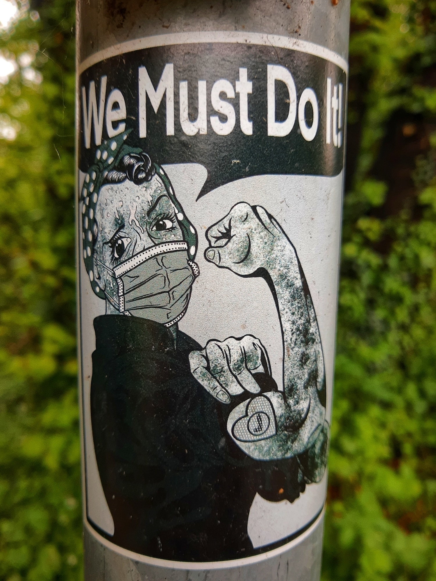 Sticker con donna con muscolo del braccio tirato ed una mascherina in volto. Sopra la scritta: We must do it
