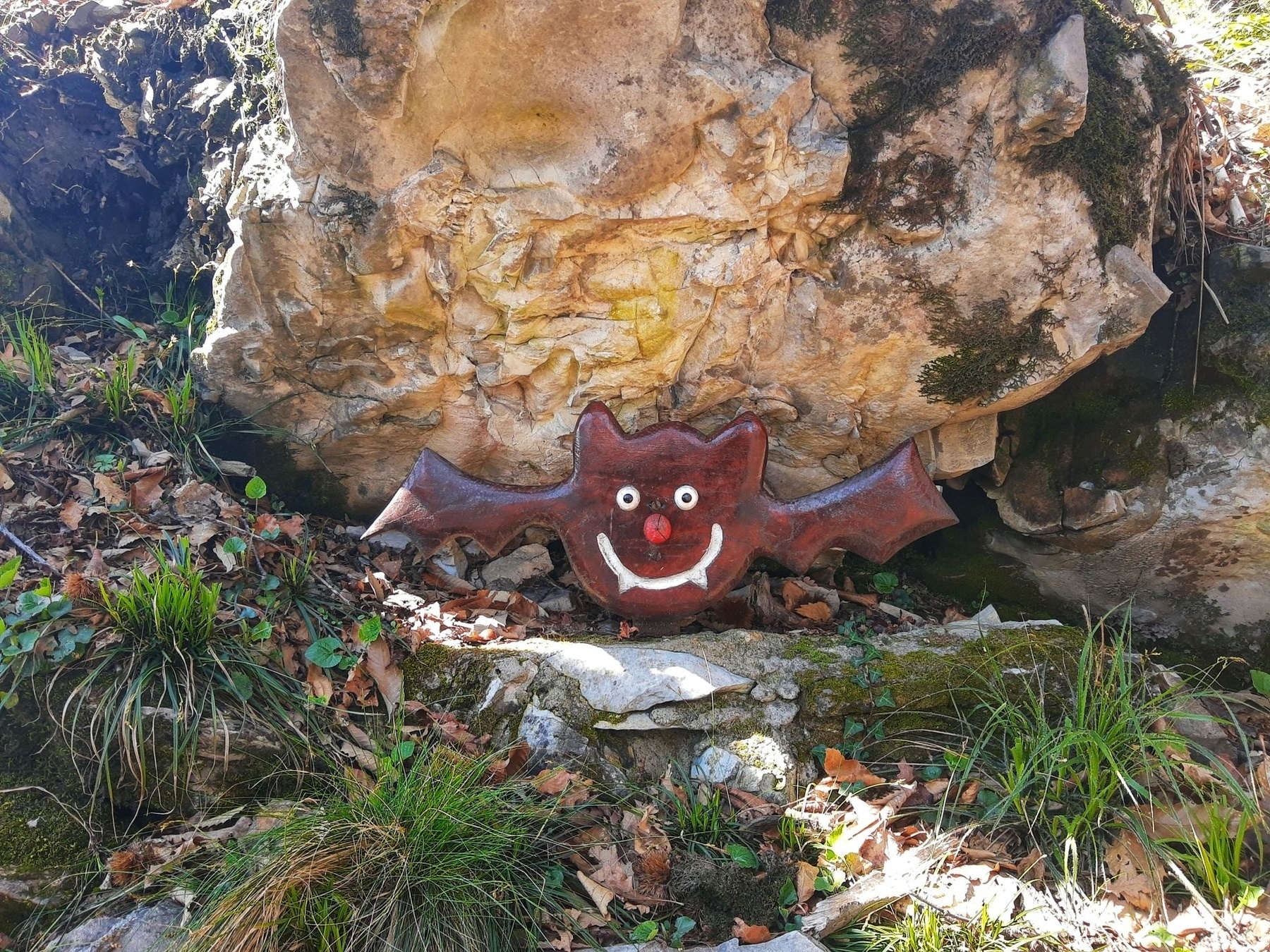 Pipistrello sorridente fatto di legno appoggiato a delle pietre