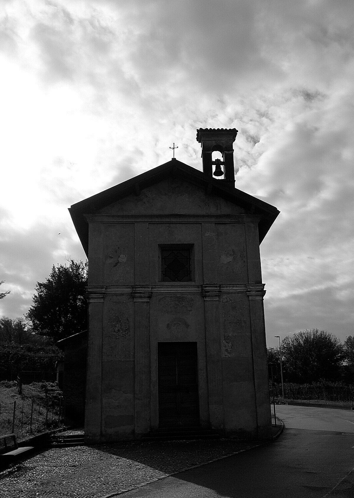 Auto-generated description: A small, old church with an ornate bell tower stands silhouetted against a cloudy sky in a peaceful rural setting.