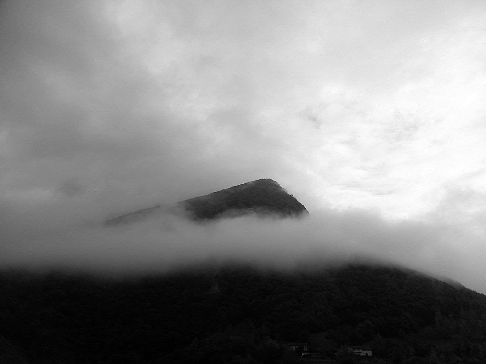 Auto-generated description: A mist-covered mountain peak rises under a cloudy sky.