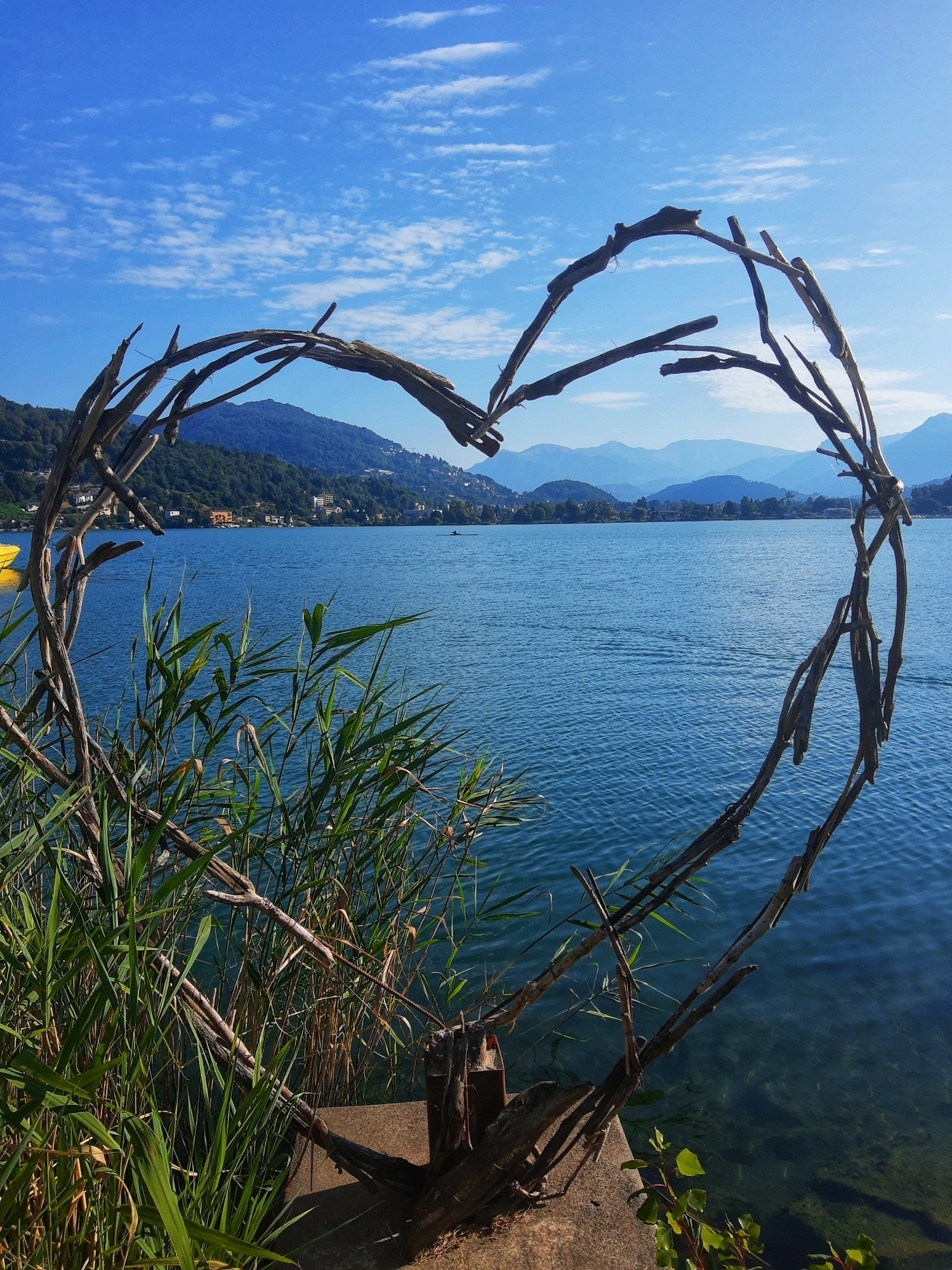 Installazione artistica con rami che formano un cuore e dietro il lago di Lugano