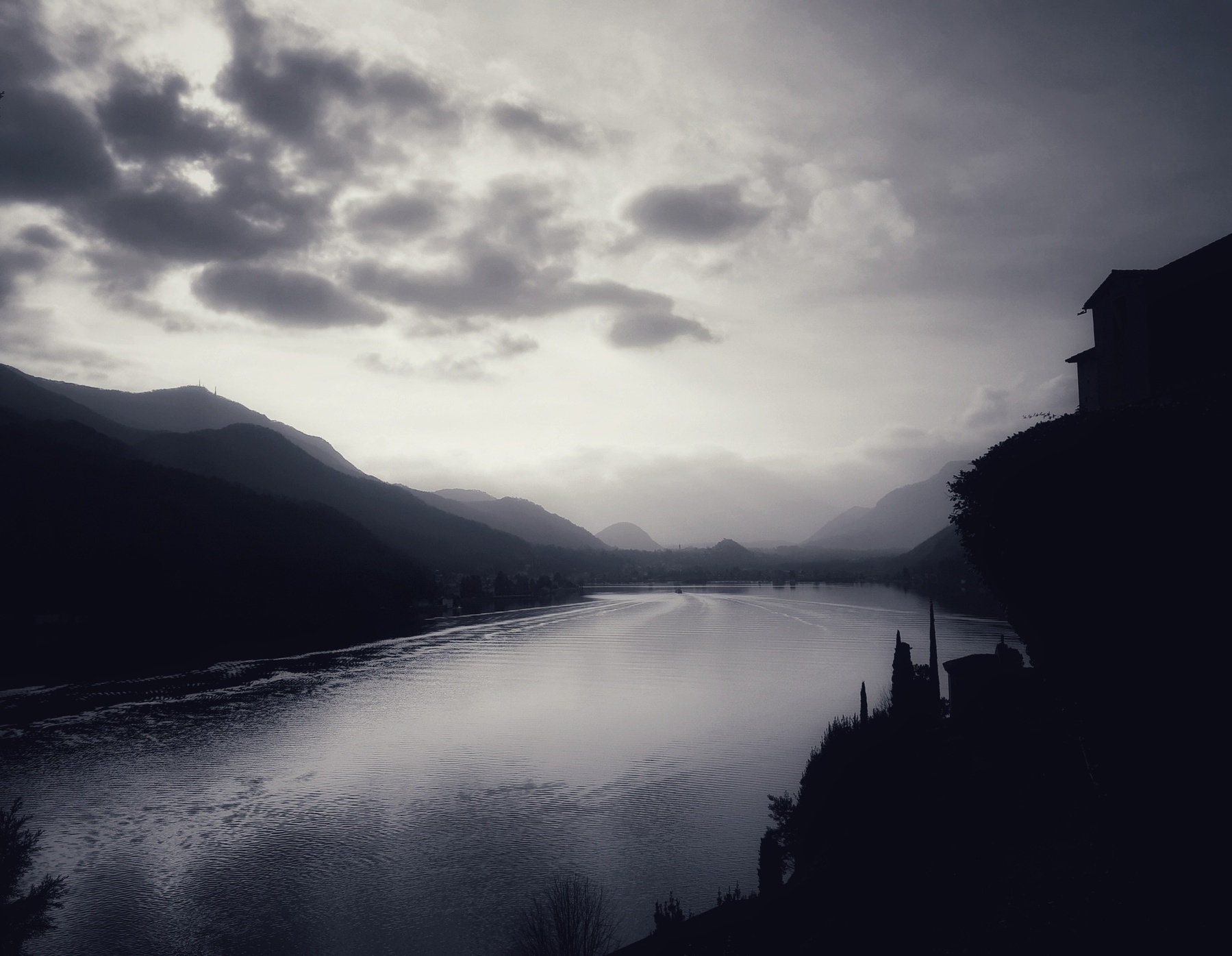 Auto-generated description: A serene lake through a misty valley surrounded by silhouetted mountains under a clouded sky.