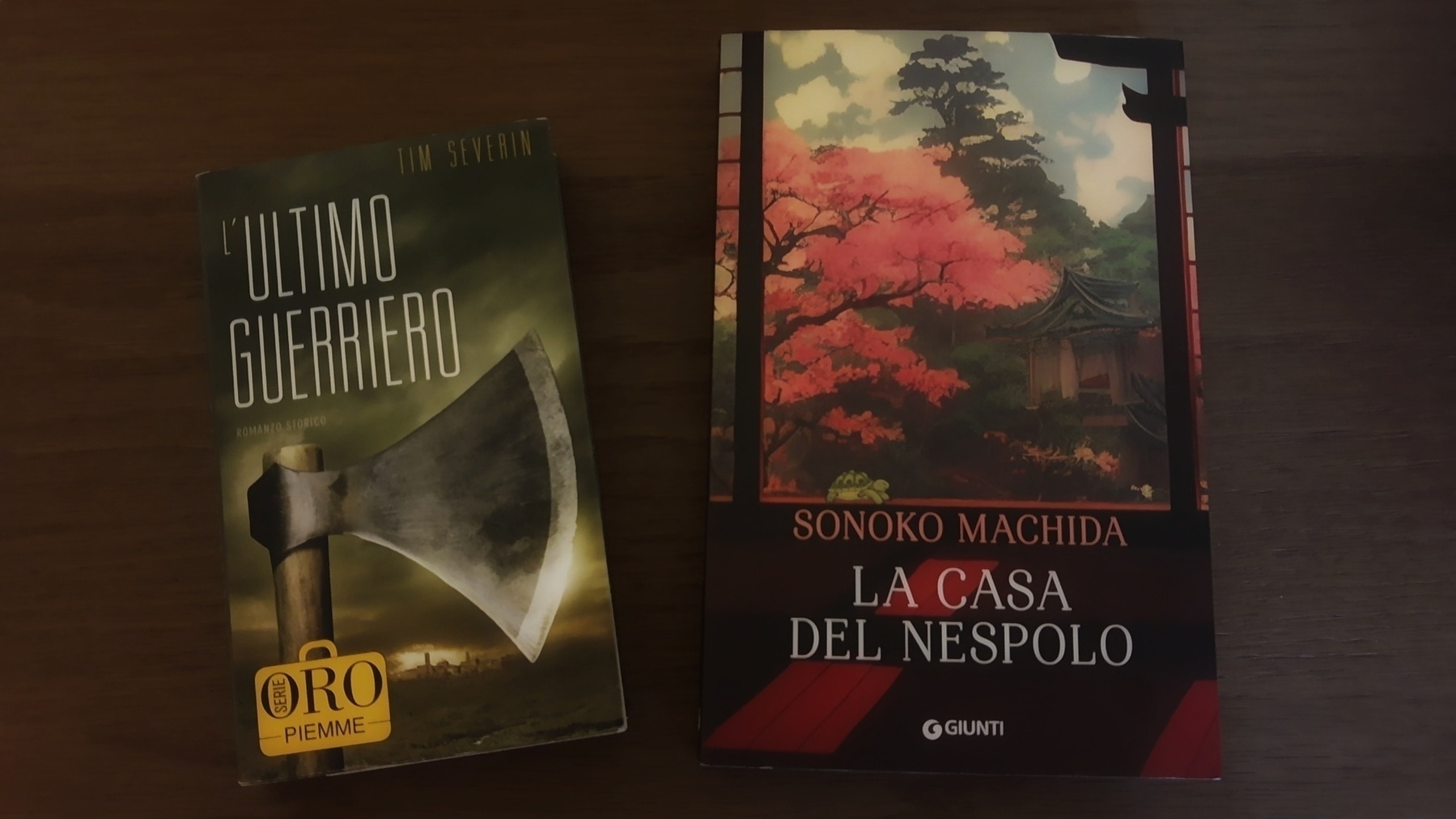 Two books, L'Ultimo Guerriero by Tim Severin and La Casa del Nespolo by Sonoko Machida, are placed on a wooden surface.