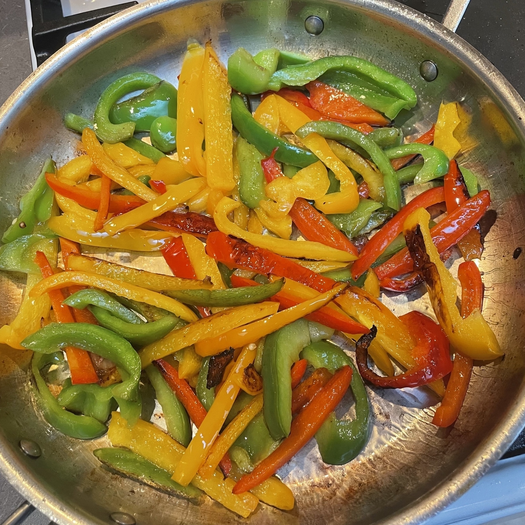 Sliced strips of yellow, greens and red peppers sautéed in a stainless steel pan. 