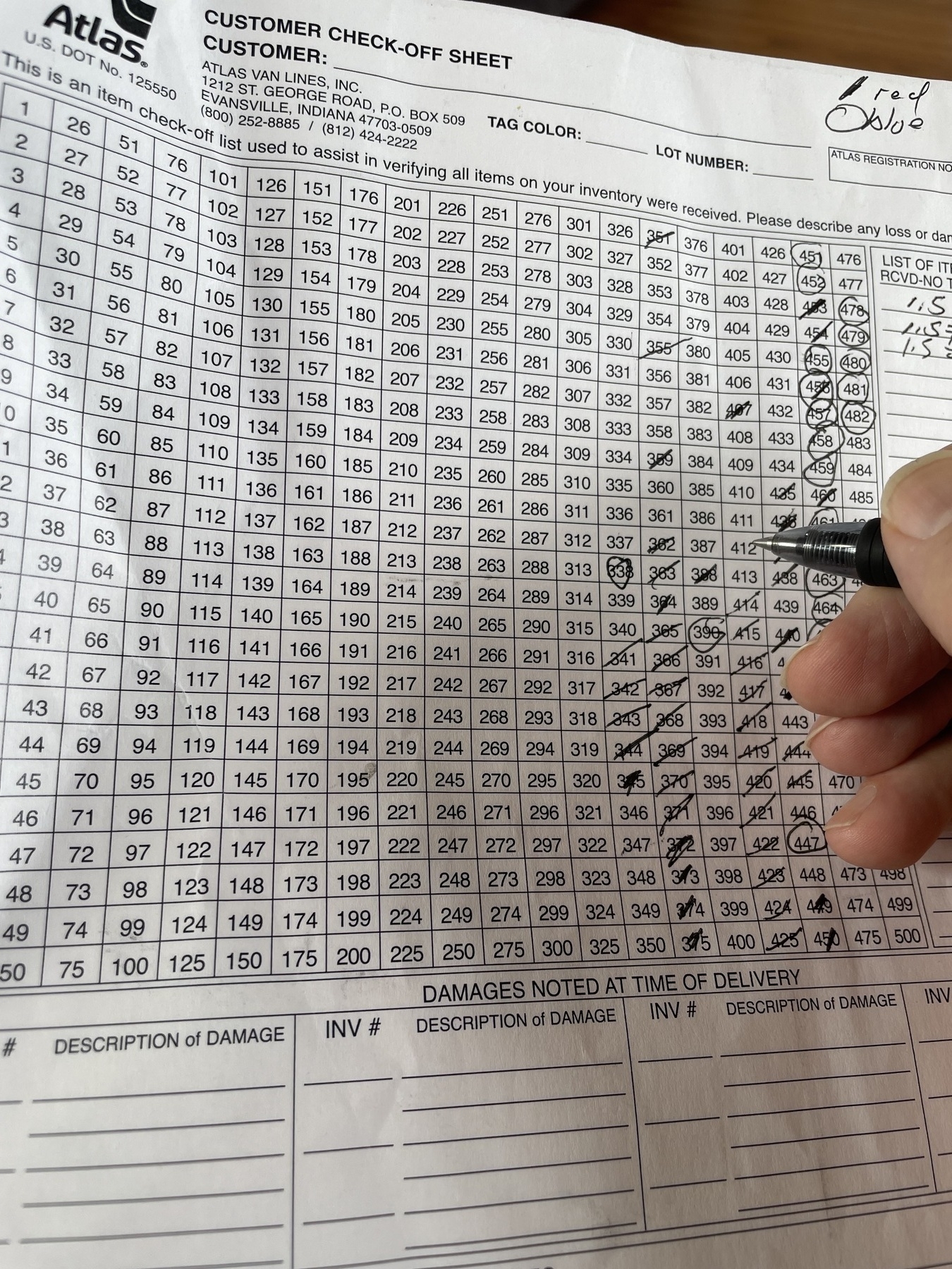 A sheet of white paper with a grid of numbers from 1-500, with a moving company logo at top, and my hand holding a pen as I mark them off. &10;