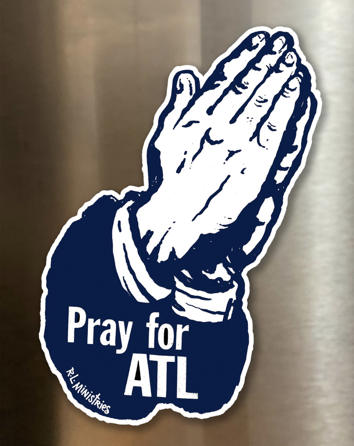 A piece of pop art by “R L Ministries” — a dark blue drawing of praying hands with the words superimposed “Pray for ATL” 