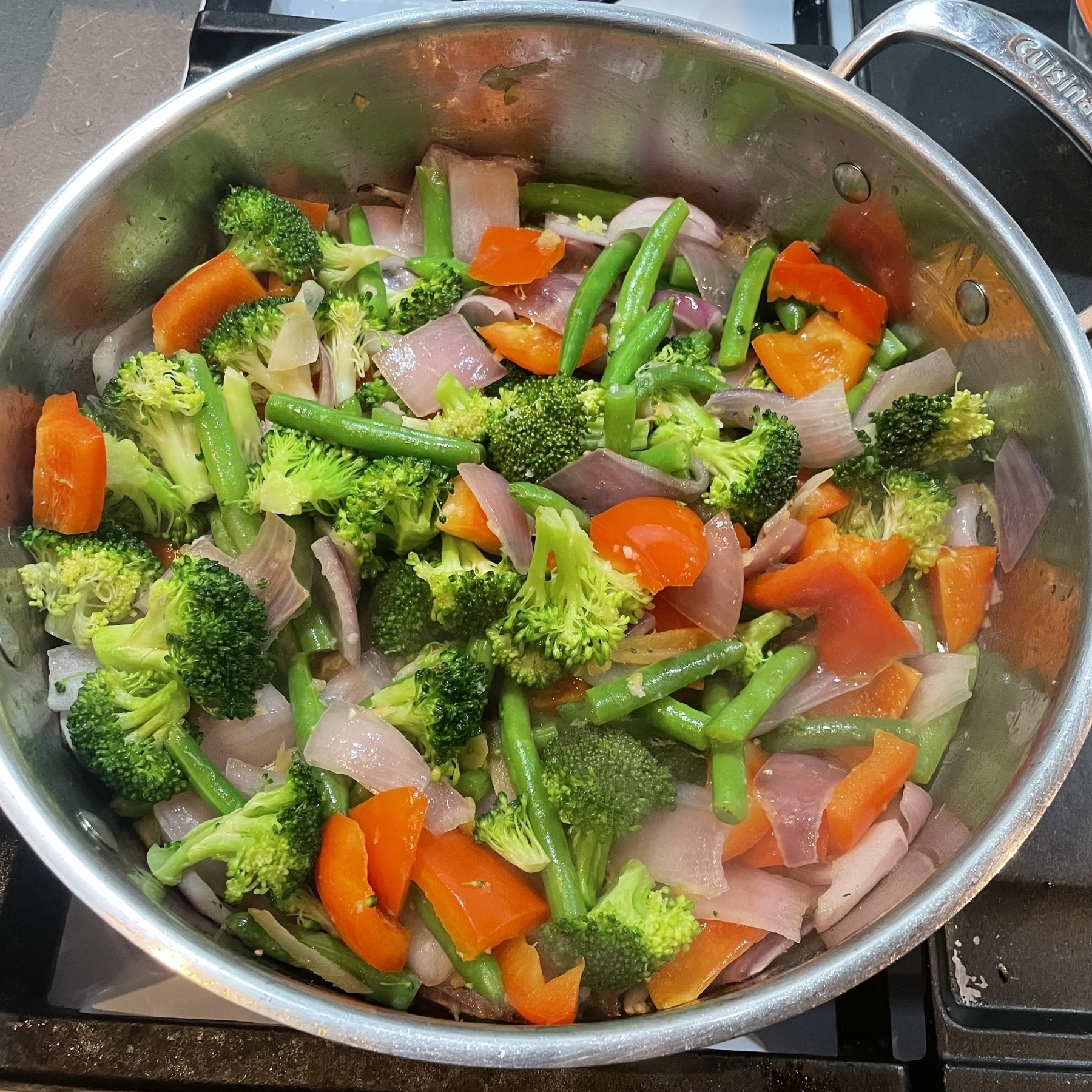 Colorful chopped vegetables in a pot starting to be cooked — red bell pepper, broccoli, green beans, onions etc. 