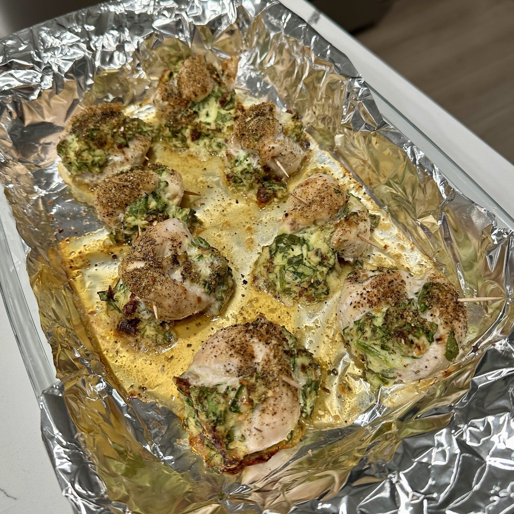 Cooked stuffed chicken breasts are arranged on a foil-lined baking tray, seasoned and golden brown.