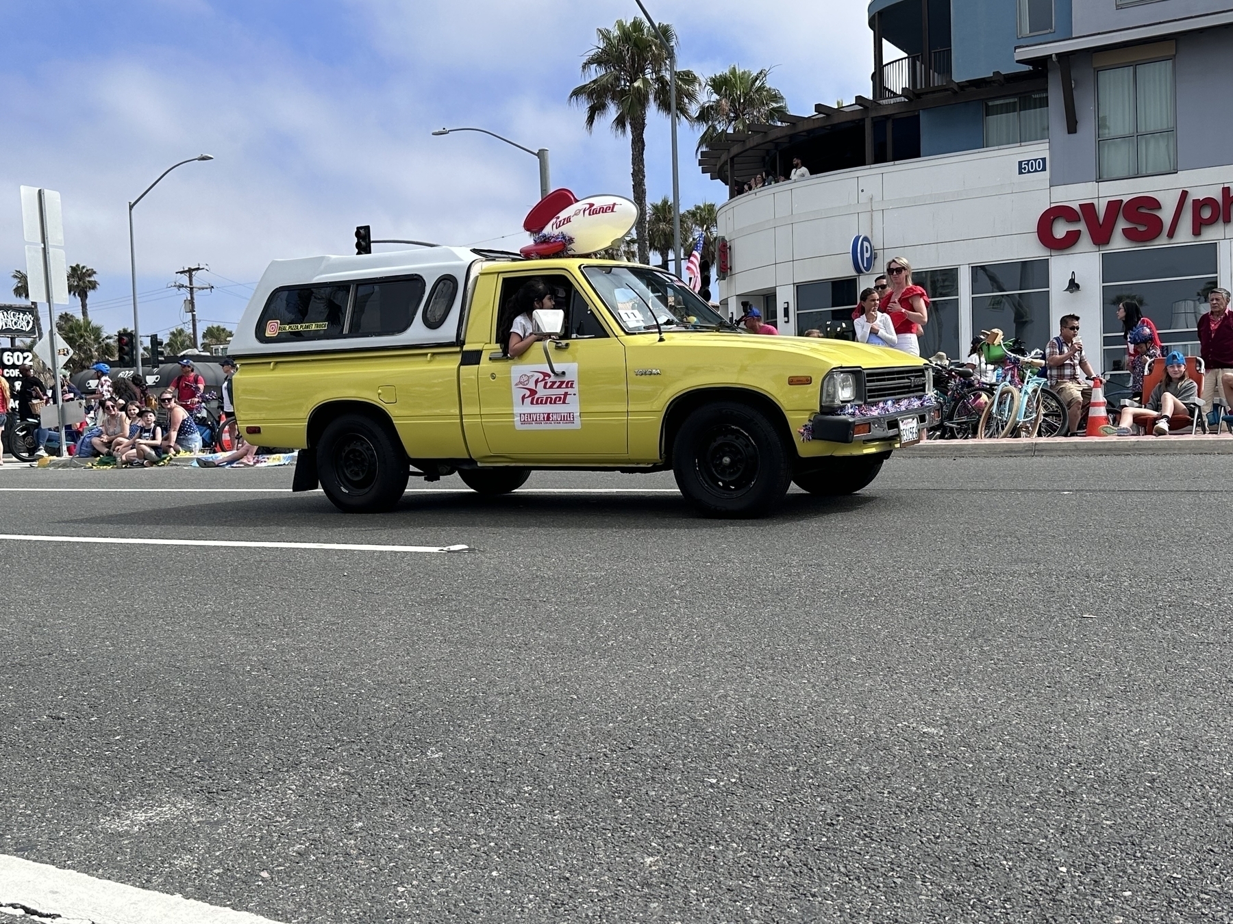 The Toy Story Pizza Planet delivery truck replica driving in a Fourth of July parade.